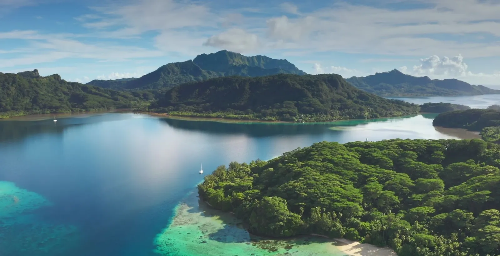 Aerial view of a deep bay between green ridges, with reef and shallows in the foreground