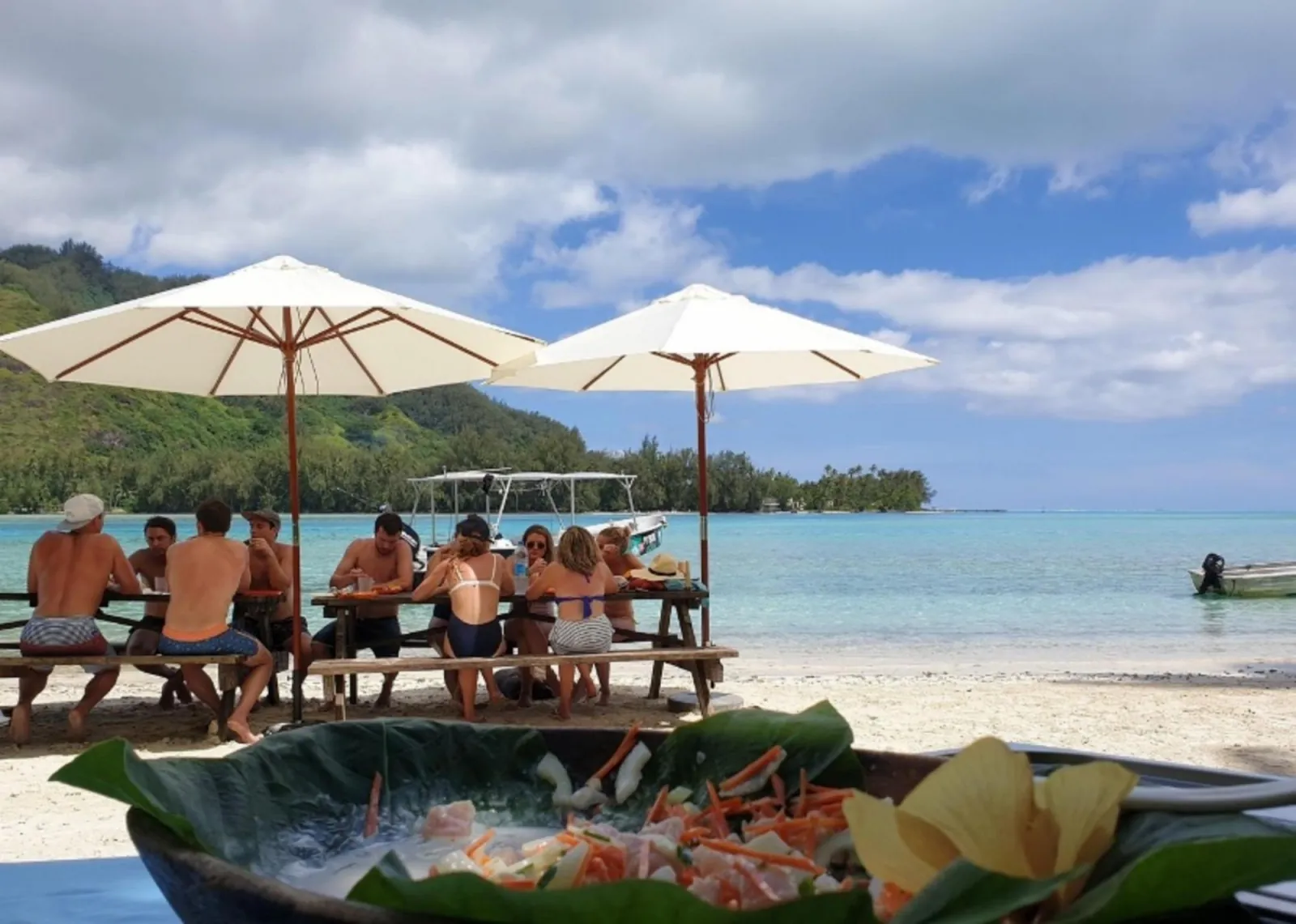 Guests eating lunch at picnic tables under umbrellas on an islet beach