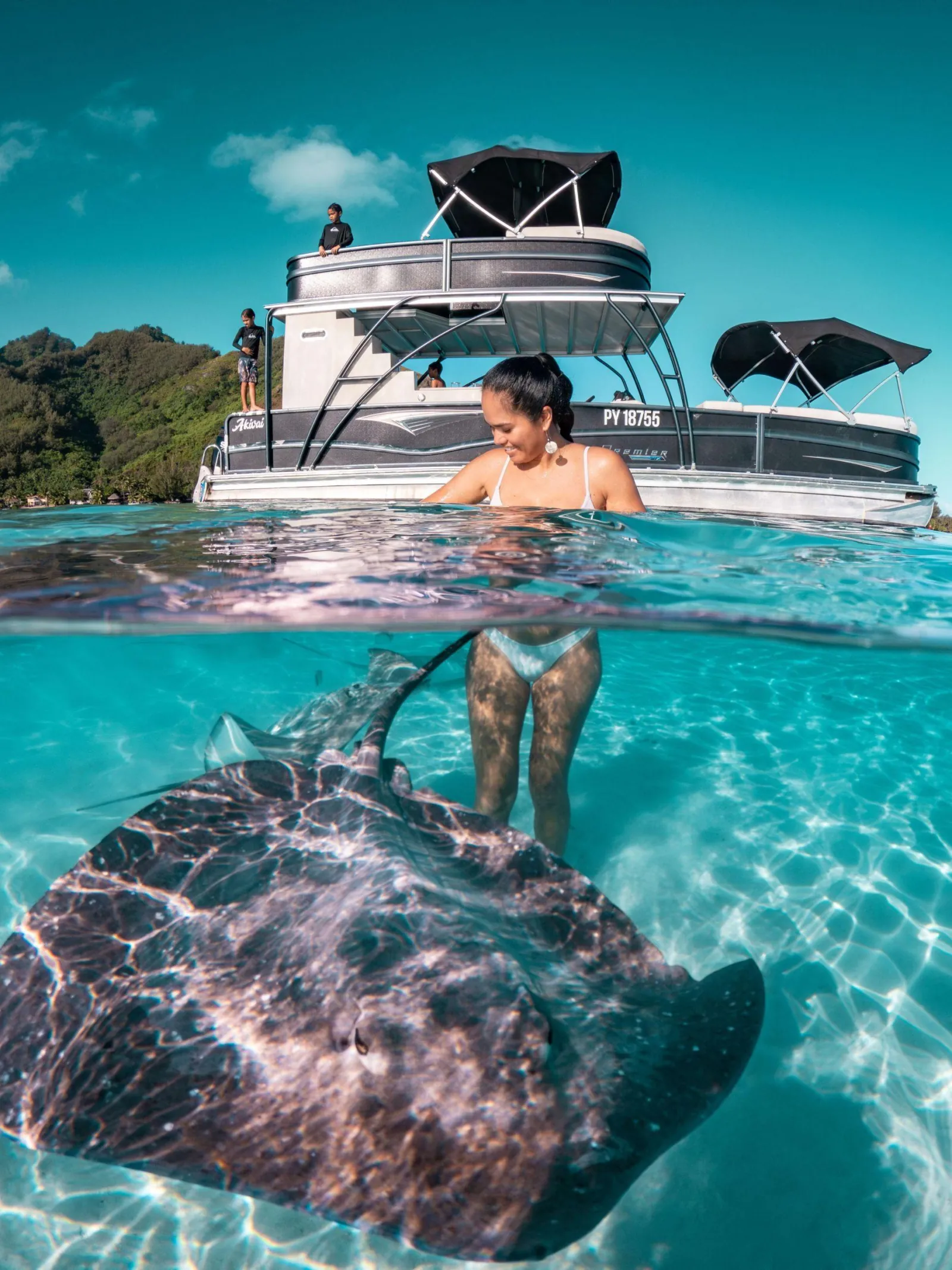 Woman standing in shallow water beside a stingray, pontoon boat behind
