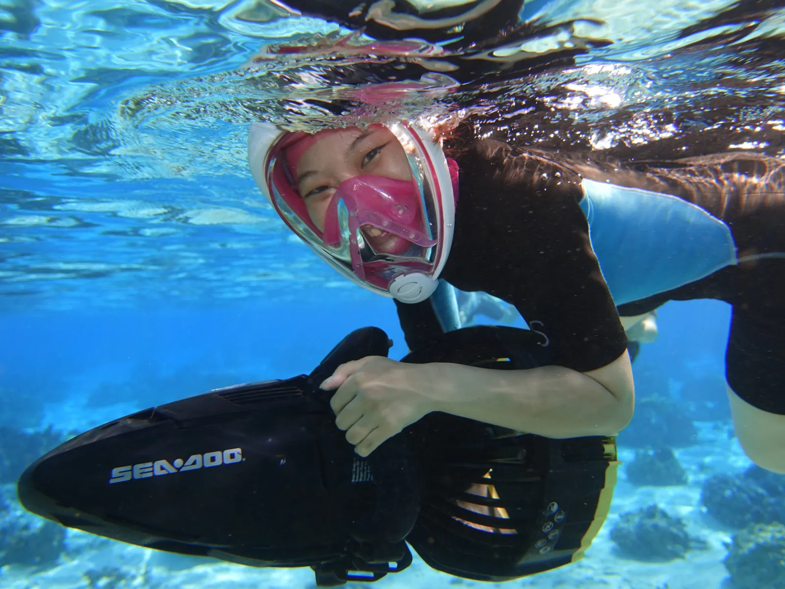 Snorkeler in a pink full-face mask holding a Sea-Doo sea scooter underwater