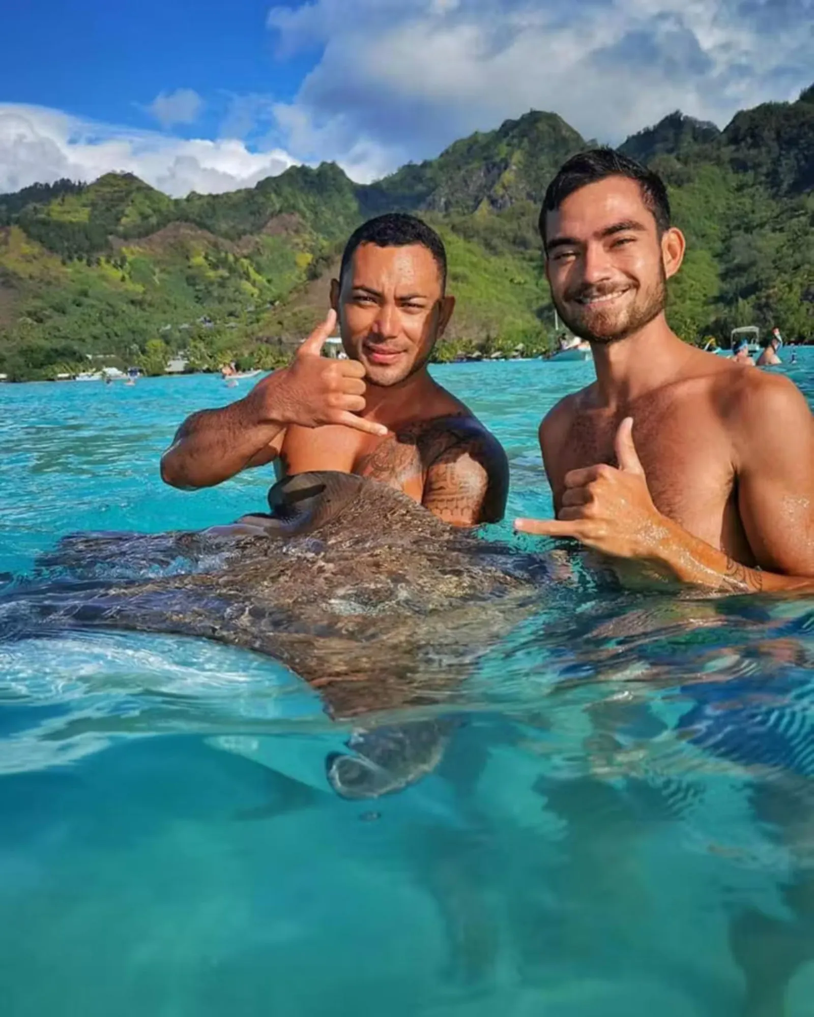 Two guides standing waist-deep in the lagoon beside a stingray