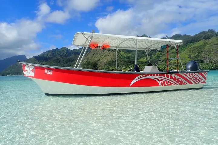 Red and white canopy boat moored in shallow turquoise lagoon water below green hills