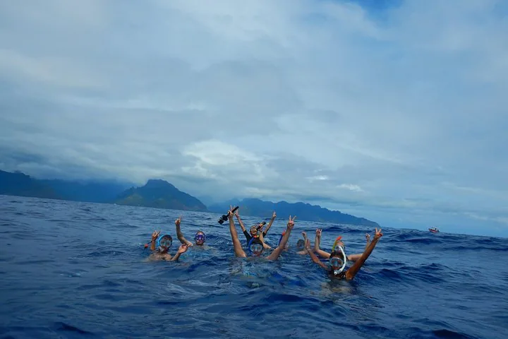 Group of snorkelers waving from the open ocean with Moorea's mountains behind
