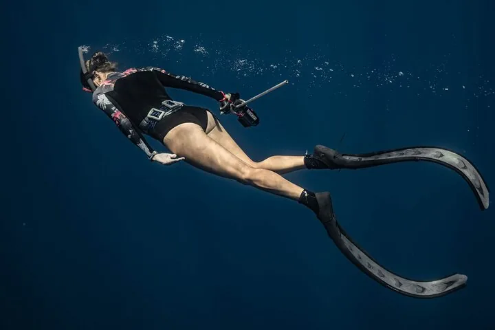 Snorkeler in long fins holding a camera in deep blue water